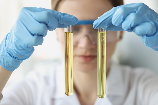 Vrouw chemicus houdt in handen twee reageerbuizen met gele transparante vloeistof voor onderzoek