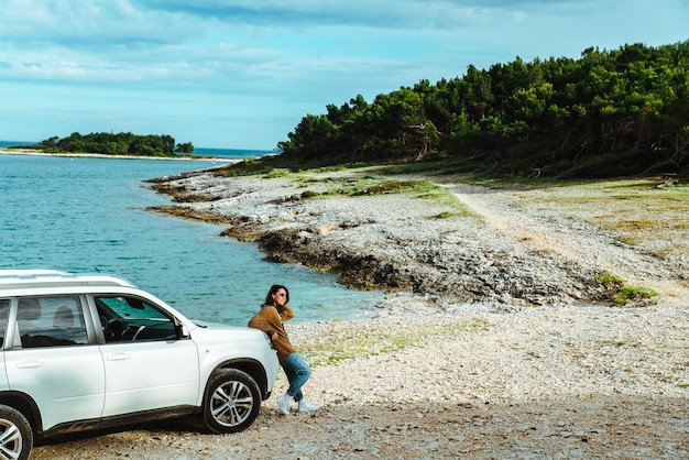 Vrouw die aan de rand van de zee staat en kijkt naar het concept van het reizen met de auto op zee