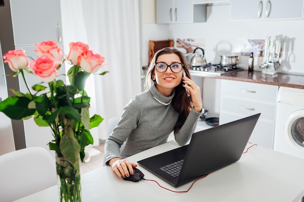 Vrouw die aan de telefoon praat en thee drinkt terwijl ze op een laptop werkt aan een moderne keuken freelancer relaxin