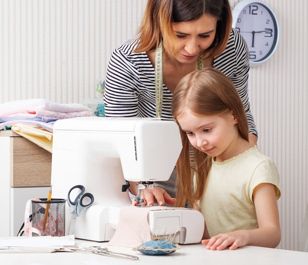 Foto vrouw die aan kind toont hoe thuis te naaien