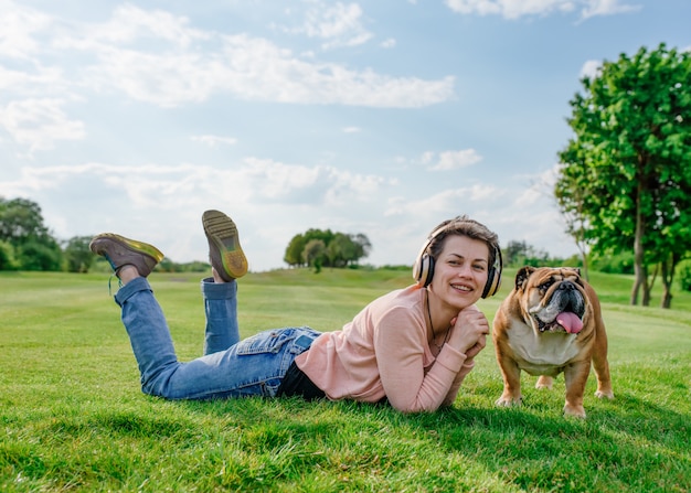 Vrouw die aan muziek luistert of audioboek en op groen gras met hond in het park rust