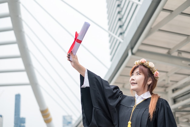 Vrouw die academische toga draagt die hand met succes opheft Bachelor Degree of University