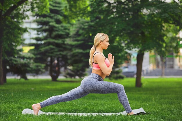 Vrouw die asana-oefeningen buitenshuis maakt. Meisje krijger pose. Stretching, wellness, rust, ontspanning, gezond, actief levensstijlconcept