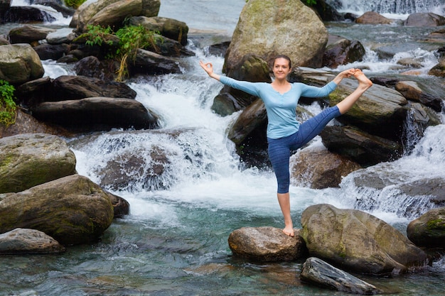 Vrouw die Ashtanga Vinyasa Yoga-asana in openlucht doet bij waterval