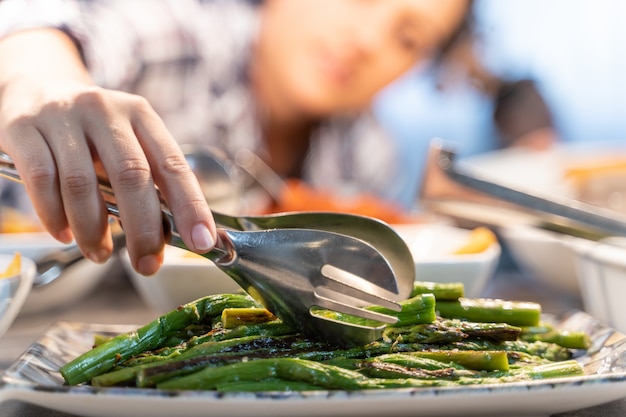 Vrouw die asperge neemt die met pincet in een zelfbedieningsrestaurant wordt gekookt