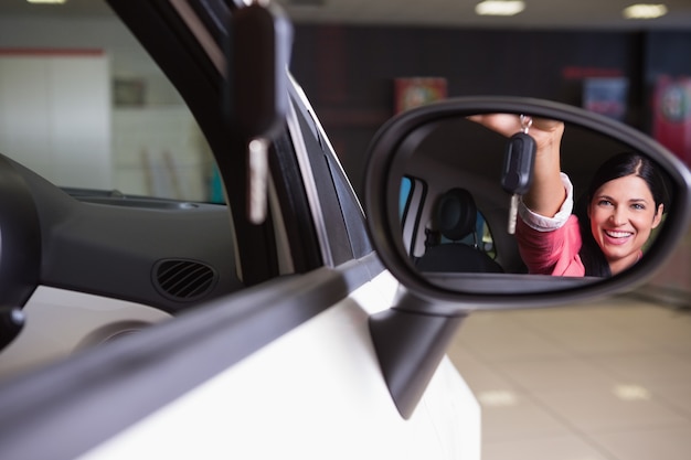 Vrouw die autosleutel in achteruitkijkspiegel toont