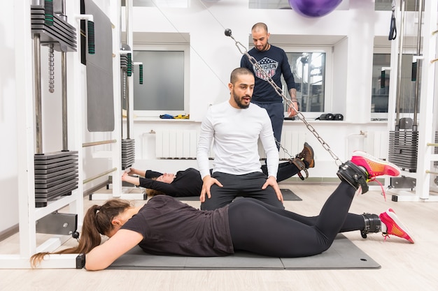 Vrouw die benen met persoonlijke trainer bij gymnastiek uitoefent