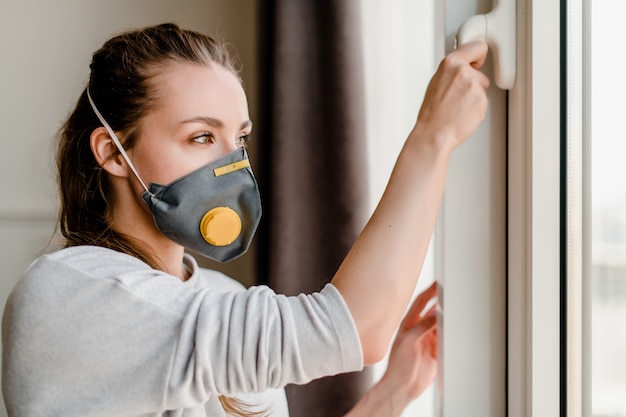 Vrouw die beschermend masker draagt dat binnen venster buiten bekijkt