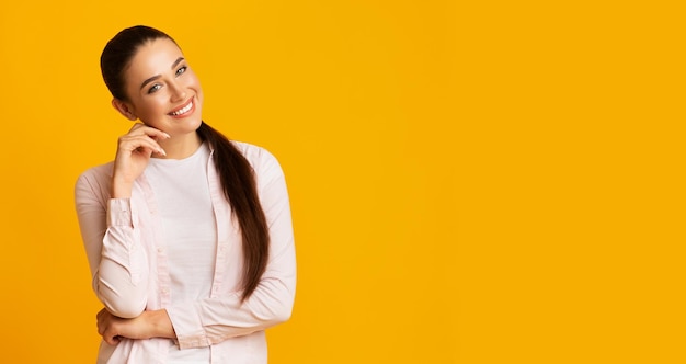 Vrouw die bij Camera glimlacht die Kin over Gele Studioachtergrond aanraakt