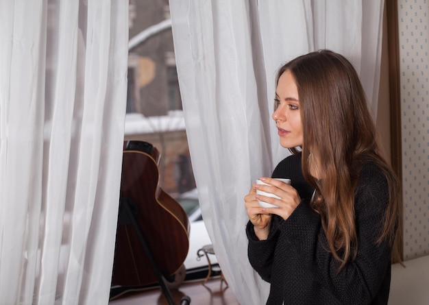 Vrouw die bij het raam staat en koffie drinkt