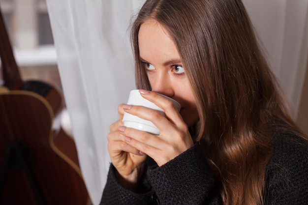 Vrouw die bij het raam staat en koffie drinkt