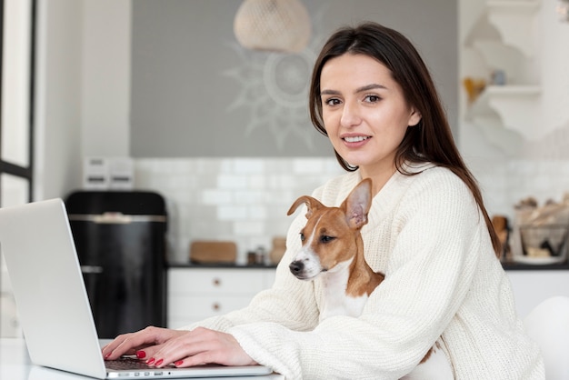 Vrouw die bij laptop met hond in haar schoot werkt