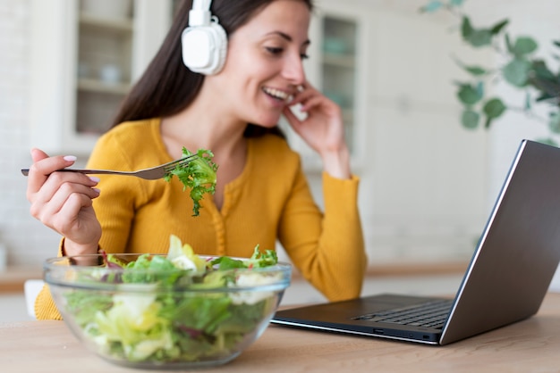 Foto vrouw die bij laptop salade eet