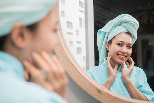 Vrouw die bij reflectie in de spiegel kijkt met een schone, frisse huid raakt in de badkamer