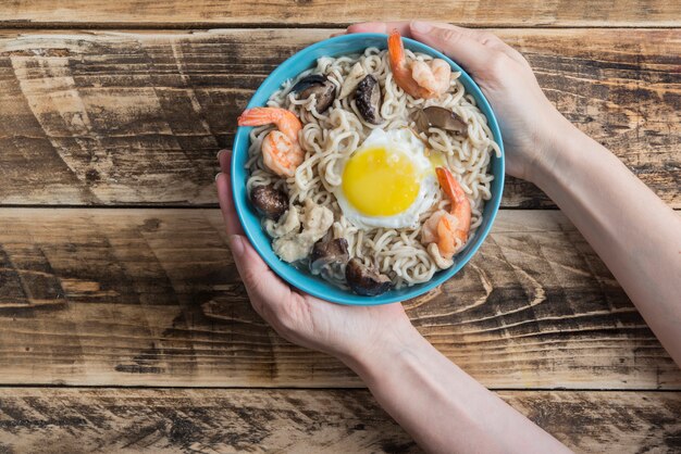 Vrouw die blauwe kom met twee handen van Udon opneemt