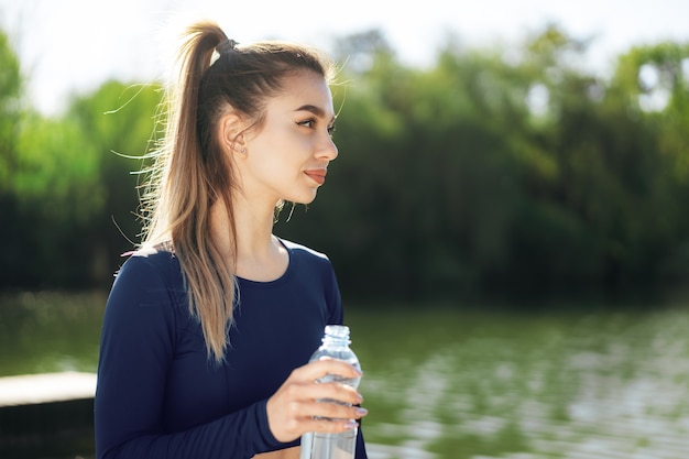 vrouw die blauwe sportkleding draagt die water drinkt in het park