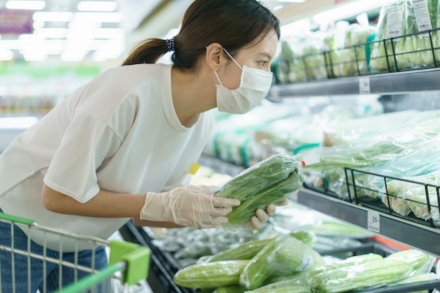 Vrouw die chirurgisch masker en handschoenen draagt, die groenten in supermarkt na pandemie coronavirus kiest.