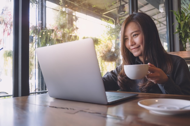 Vrouw die computerlaptop met koffiekop gebruikt