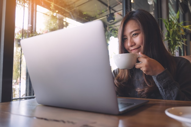 Vrouw die computerlaptop met koffiekop gebruikt