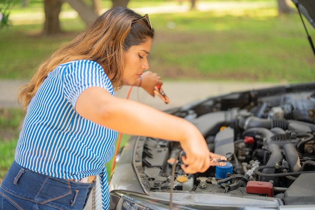 Foto vrouw die de batterij van haar voertuig op straat repareert terwijl ze op een sleepwagen wacht