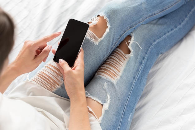 Vrouw die de celtelefoon controleert op het bed