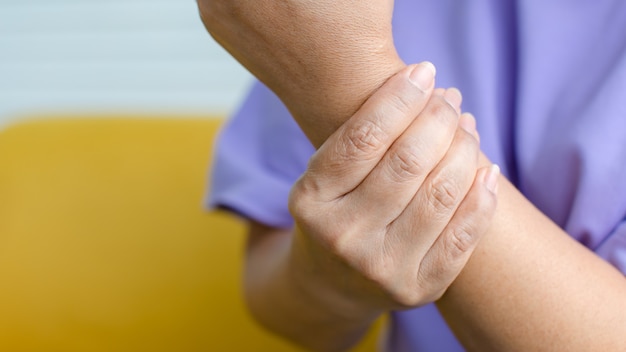 Vrouw die de hand gebruikt om andere op de arm te houden en pijn voelt, lijdt, pijn doet en tintelt. concept van guillain barre-syndroom en gevoelloze handenziekte.