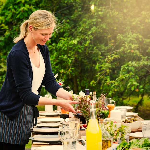 Vrouw die de lijst voor een diner in de tuin voorbereidt