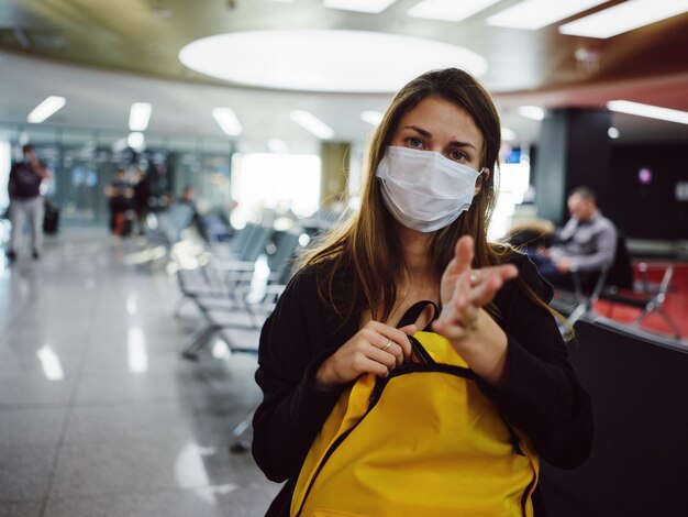 Vrouw die de luchthaven van de medische masker gele rugzak draagt die op vlucht wacht