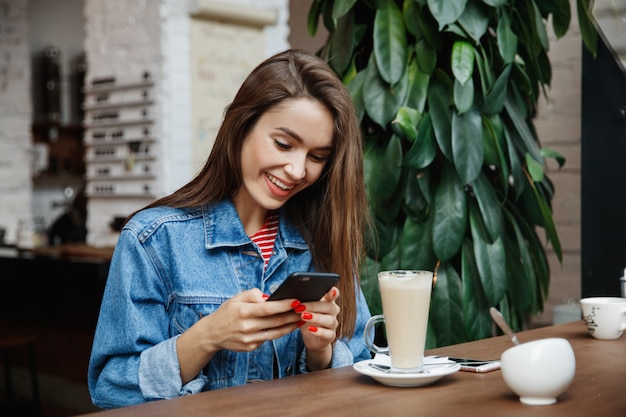 Vrouw die de telefoon in een koffiewinkel bekijkt