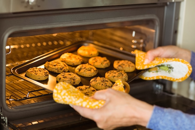 Vrouw die dienblad van verse koekjes nemen uit oven