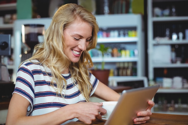 Vrouw die digitale tablet gebruiken terwijl het hebben van kop van koffie