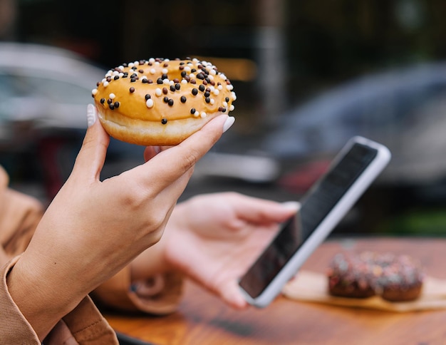 Vrouw die donuts eet en naar de telefoon kijkt