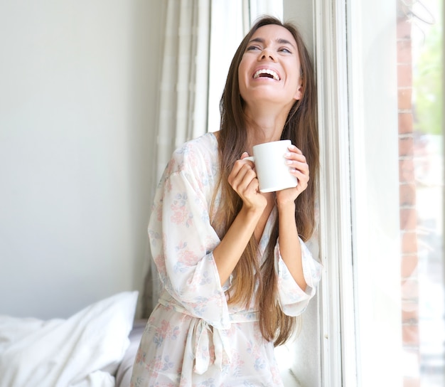 Vrouw die door venster het drinken koffie glimlacht