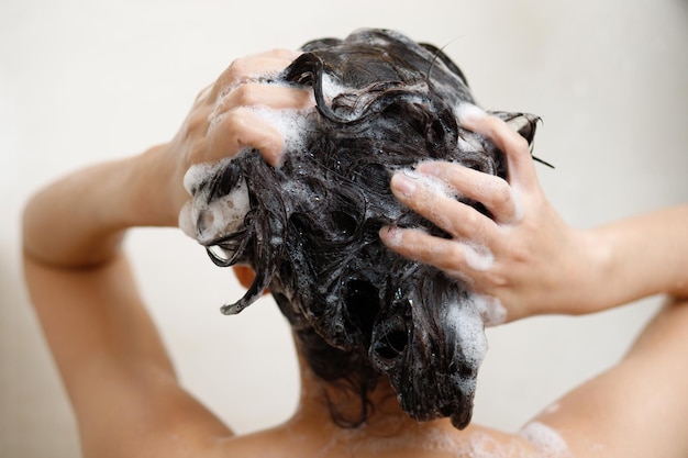 Vrouw die douche neemt en haar wast met shampoo in de badkamer thuis