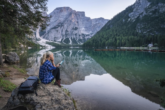 Vrouw die ebook leest in Pragser Wildsee met weerspiegelde bergen op de oppervlakte van het meer Dolomieten Italië