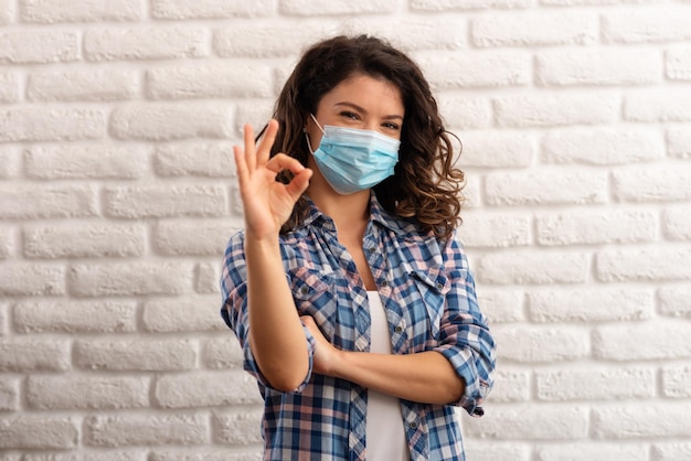 Vrouw die een beschermend masker draagt en een OK-teken toont Vrouw die een chirurgisch masker draagt voor het coronavirus