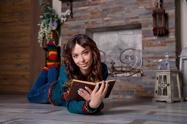 Vrouw die een boek leest en geniet van een warme chocolademelk bij de open haard, liggend op de vloerverwarmde vloer fl