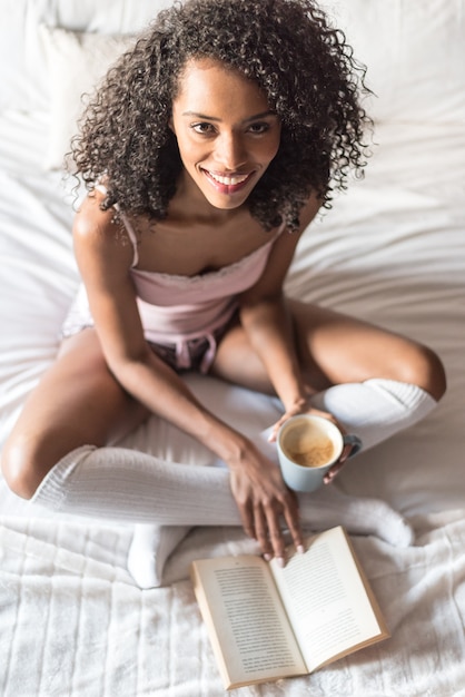 Vrouw die een boek leest en koffie op bed met sokken drinkt