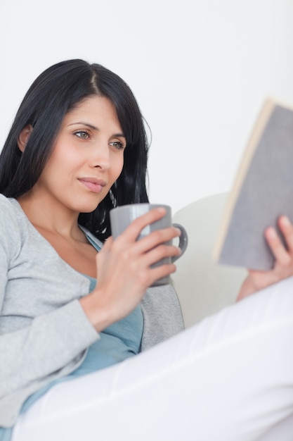 Vrouw die een boek leest terwijl het houden van een grijze mok