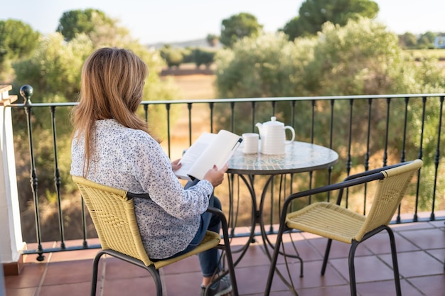 Vrouw die een boek leest zittend op een terras met uitzicht op de buitenkant op een rustige en ontspannen dag