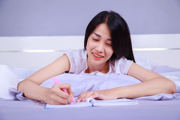 vrouw die een boek op haar bed in de slaapkamer schrijft