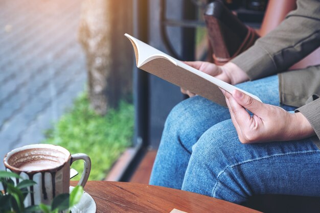 vrouw die een boek opent om te lezen met notitieboekjes en koffiekopje op houten tafel in café