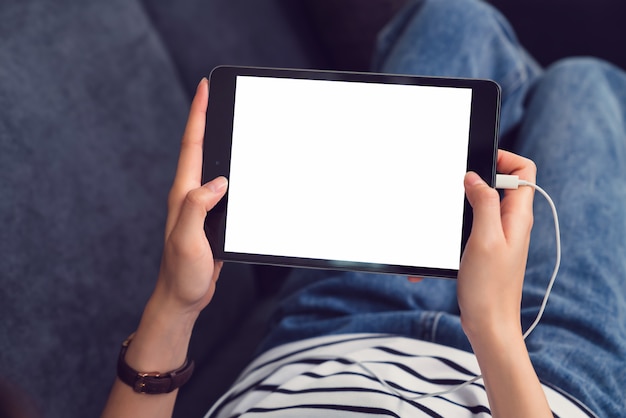 Vrouw die een digitaal tabletmodel van het lege scherm houden en levensstijl op bank in het huis gebruiken.