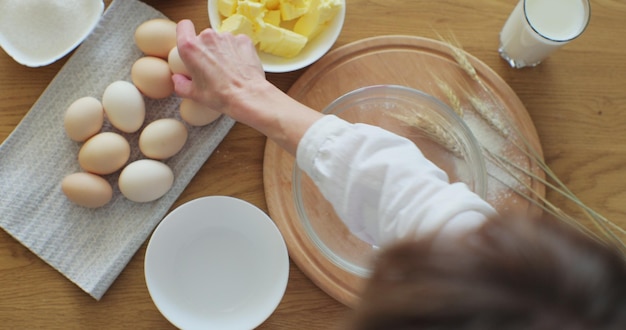 Vrouw die een ei tot meel kraakt om brood te maken volgens traditioneel recept Vrouw die thuis bakt en geniet van hobby