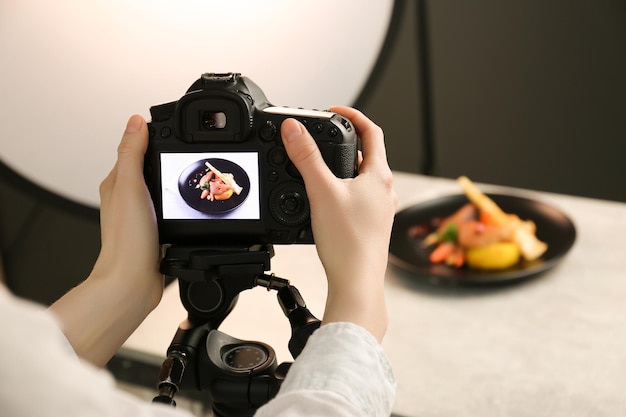 Vrouw die een foto maakt van een gerecht met kip, pastinaak en aardbeien op een grijze tafel in een professionele fotostudio close-up food stylist