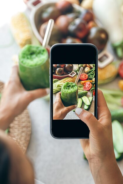 Foto vrouw die een foto maakt van een smoothie op haar smartphone van dichtbij