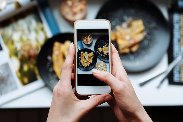 Vrouw die een foto maakt van het ontbijt met smartphonehanden houdt de telefoon van boven vast