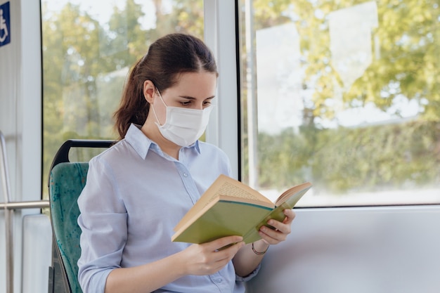 Vrouw die een gezichtsmasker draagt en een boek leest tijdens het reizen met het openbaar vervoer