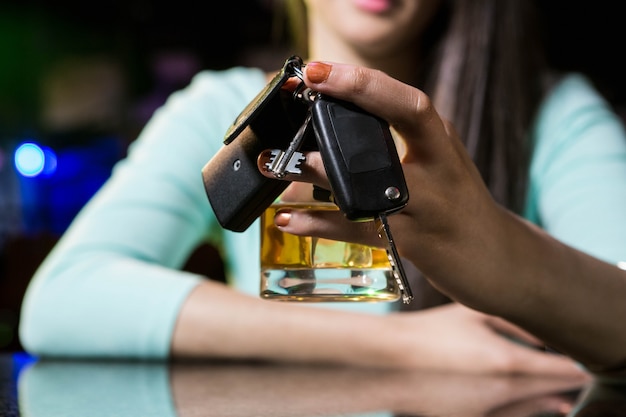 Vrouw die een glas whisky en autosleutels houdt bij barteller