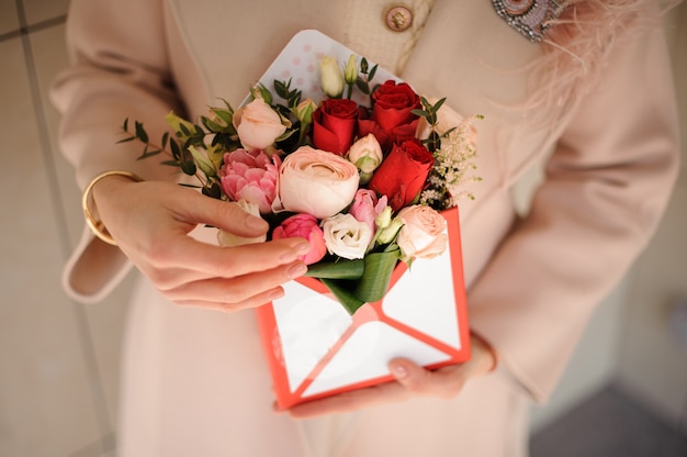 Vrouw die een kleine doos tedere roze en hartstochts rode bloemen houdt